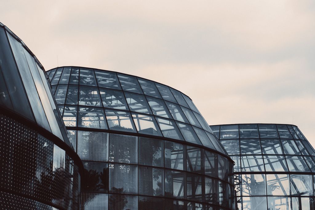 Architectural photo of futuristic glass dome buildings with metal frames on a cloudy day.
